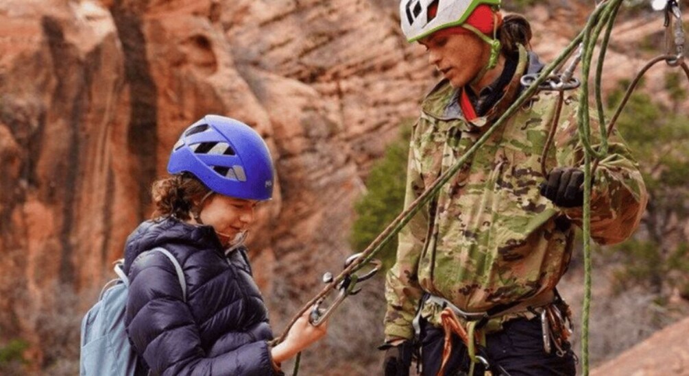 Two people engaged in a climbing activity with ropes and harnesses, set against a rocky cliff backdrop. 5