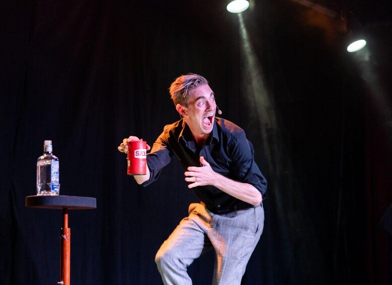 A person on stage with a microphone, holding a red can labeled 'SAX' and a bottle. 4