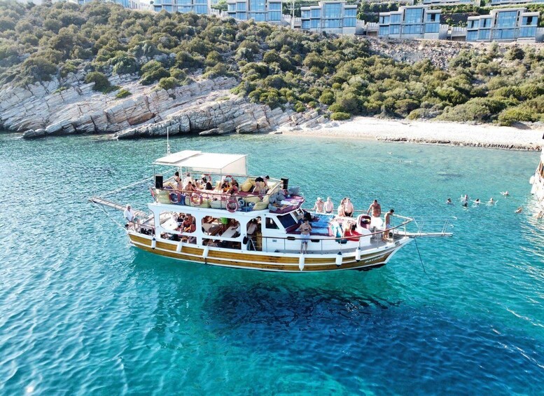 A boat with passengers on a turquoise sea, surrounded by rocky cliffs and buildings. 1