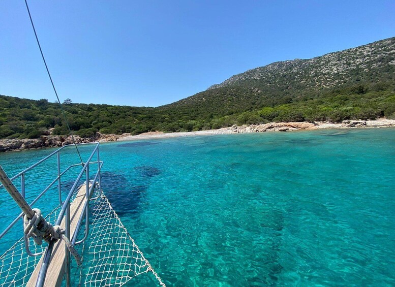 A boat on clear turquoise water with a rocky beach and green hills in the background. 2