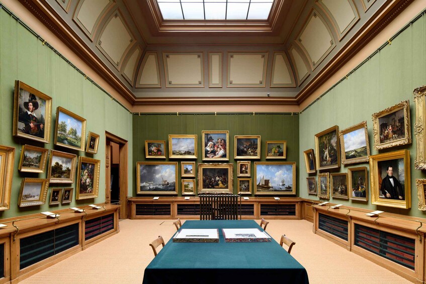 A gallery with paintings on the walls and a long table in the center. 4