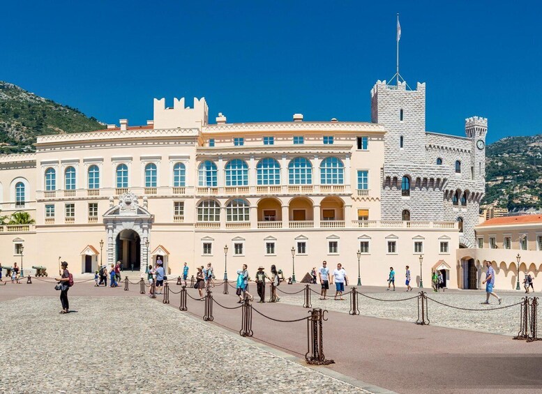 A historic building with a prominent tower and a castle-like structure, surrounded by a cobblestone plaza with people walking. 3