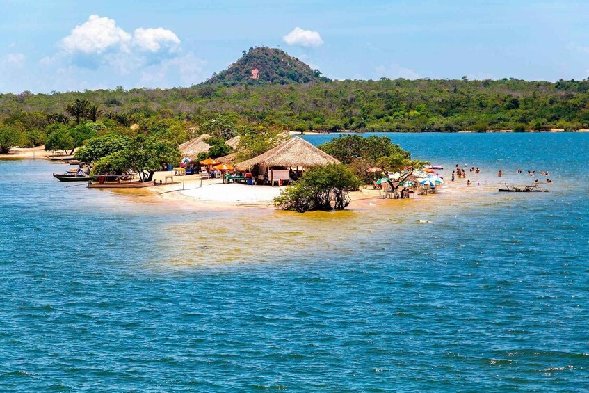 A beach with thatched-roof huts, a small island with trees, and a hill in the background. 3
