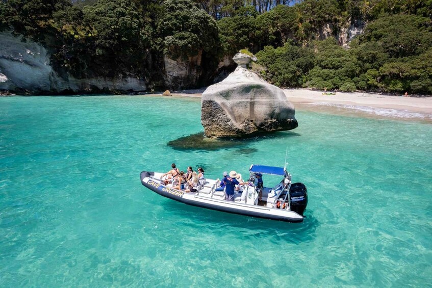 A boat with passengers near a large rock formation surrounded by clear turquoise water and a forested coastline. 1