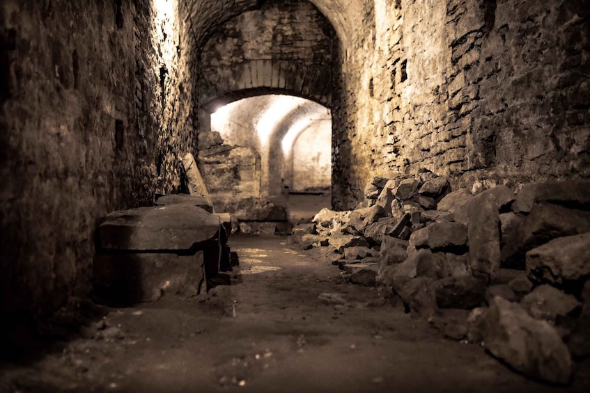 An ancient stone tunnel with rough walls and scattered debris. 1