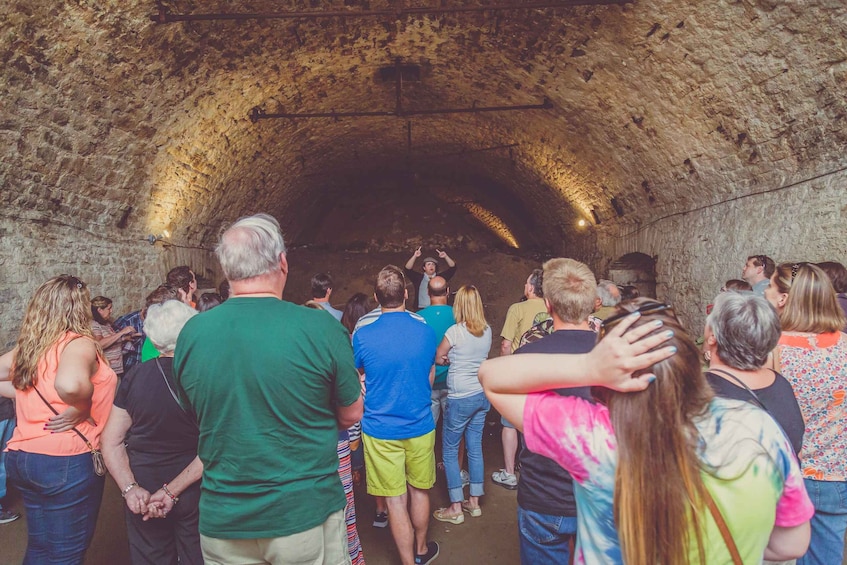 Eine Gruppe von Menschen steht in einem steinhöhlenartigen Tunnel. 1