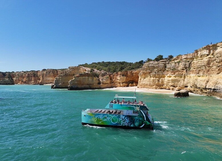 A boat with passengers on a turquoise sea, cliffs, and a sandy beach. 3