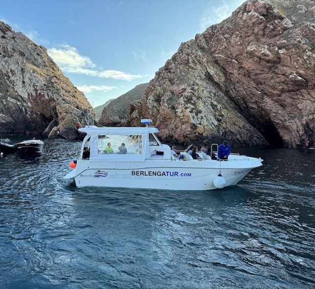 A white boat named 'BERLENGATUR.COM' with passengers, navigating through a rocky coastal area. 2