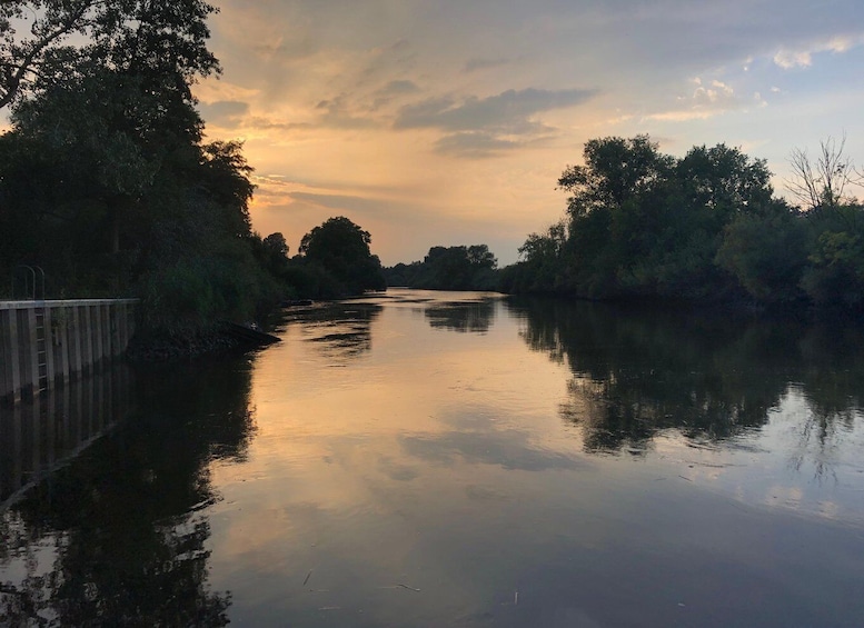 A calm river at sunset with trees on both sides and a bridge in the foreground. 5