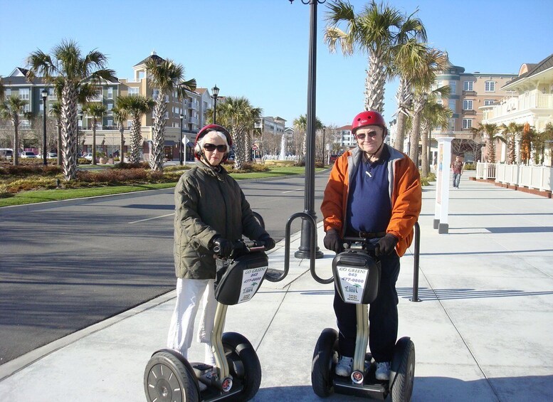 Two people on Segways in a sunny urban area with palm trees and buildings. 1