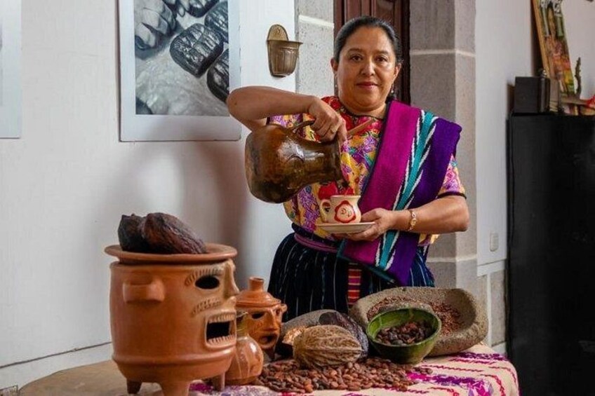 A person pouring liquid from a jug into a ceramic cup, surrounded by various pottery items. 1