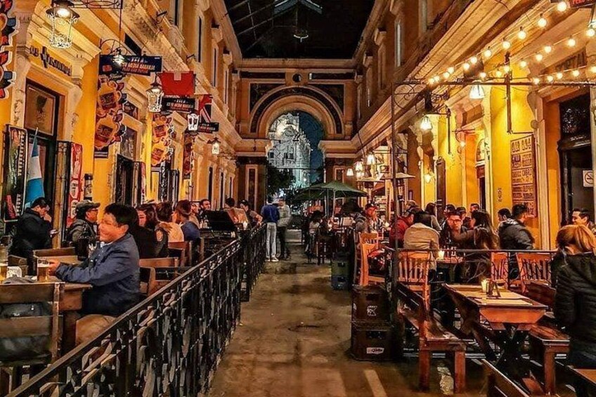 A bustling indoor market with people dining at tables, a central archway, and various signs and decorations. 5