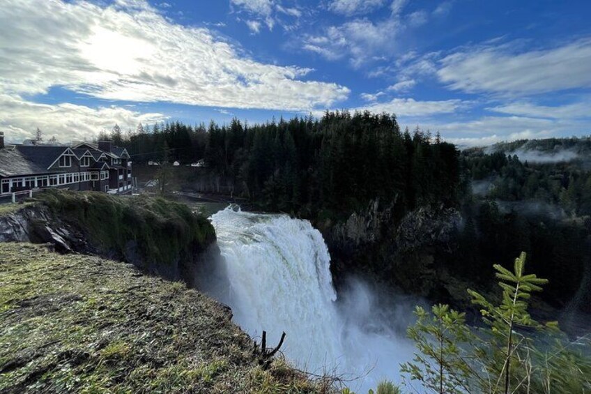 A waterfall cascading down a rocky cliff, surrounded by dense forest and a building in the background. 2