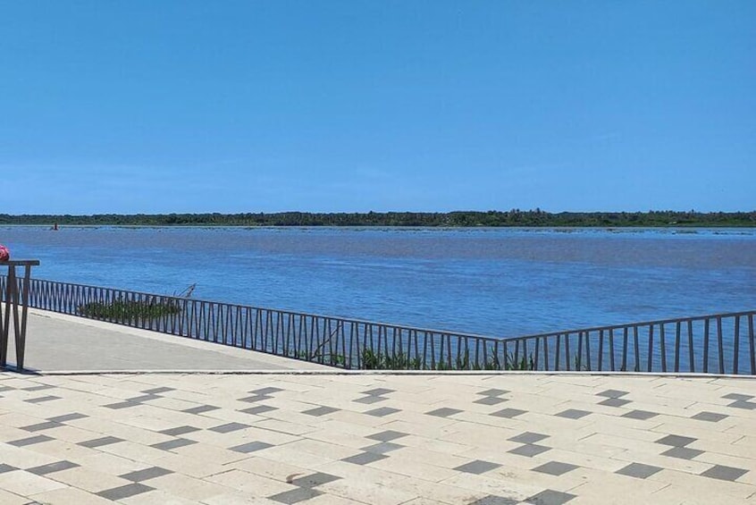 A paved walkway with a railing overlooking a calm body of water. 1