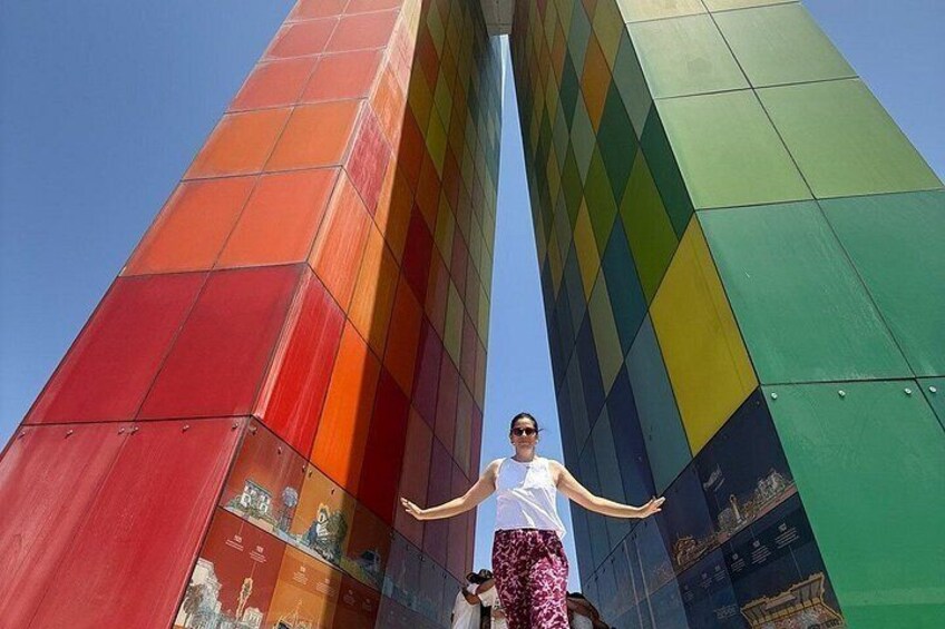 A person standing in front of a tall, colorful building with a clear sky in the background. 1