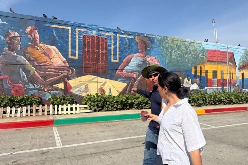 A mural with people and buildings, a white fence, and a road. 3