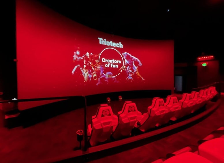 A red-lit theater with a screen displaying 'Triotech' and 'Creators of fun'. 3