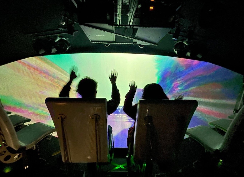 Two people seated facing a large, colorful projection screen. 4