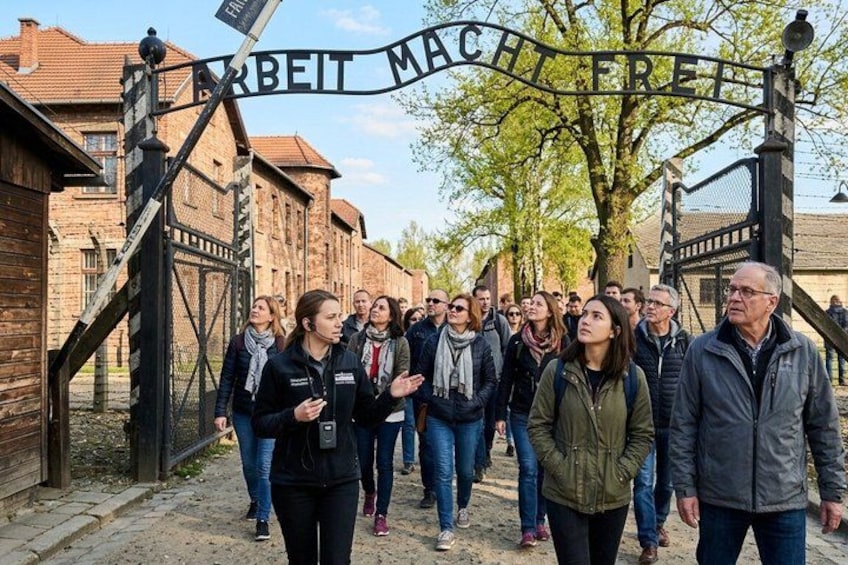 A group of people walking in front of a gate with the inscription 'ARBEIT MACHT FREI'. 5