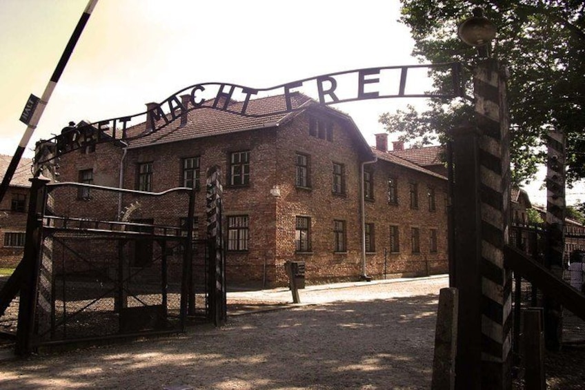 A brick building with a sign that reads 'MACHBETREI' and a metal gate in front. 2