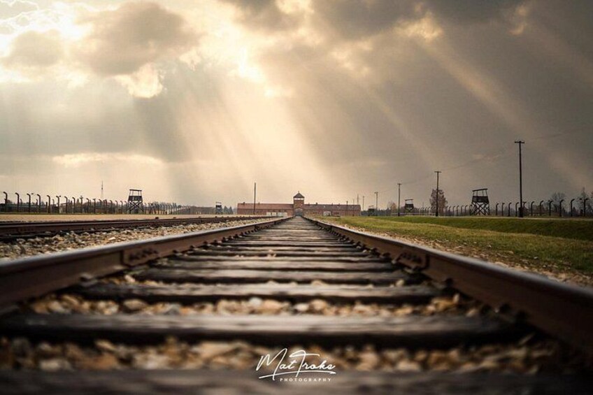 Vías de tren que se dirigen hacia un edificio lejano bajo un cielo nublado. 4