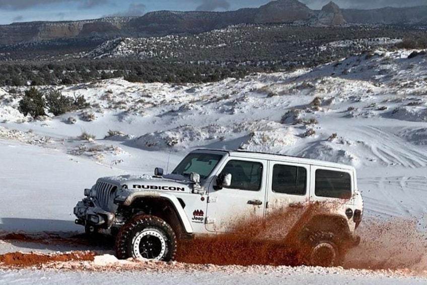 Un véhicule tout-terrain blanc roule sur un terrain enneigé, avec un paysage accidenté en arrière-plan. 2