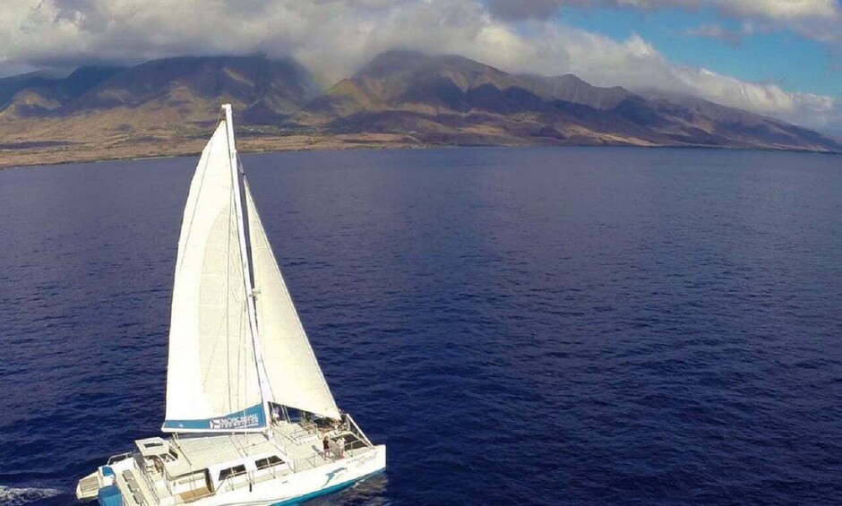 A sailboat on a calm sea with mountains in the background. 1