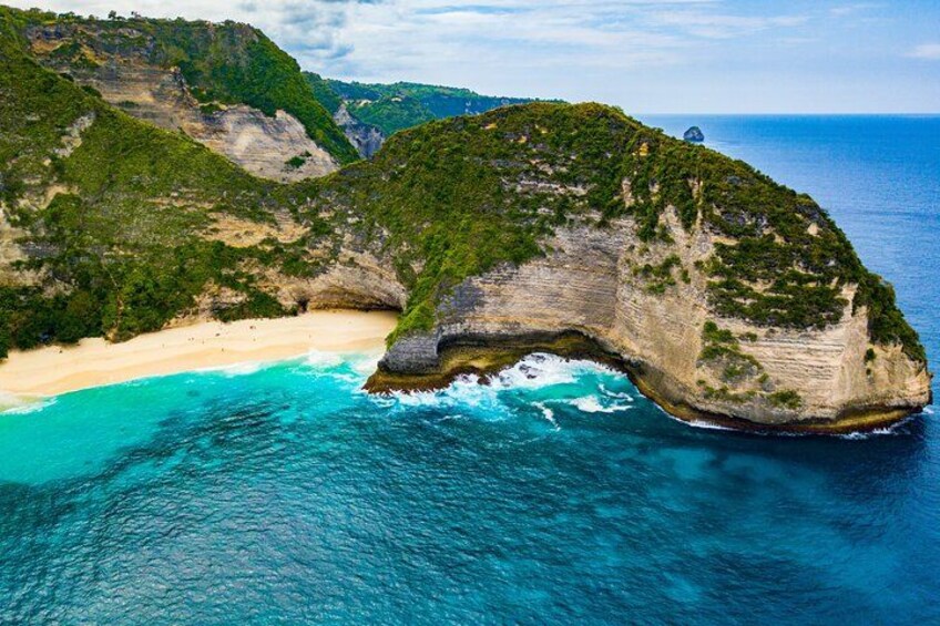 A coastal landscape with a prominent rock formation, a sandy beach, and clear turquoise waters. 2