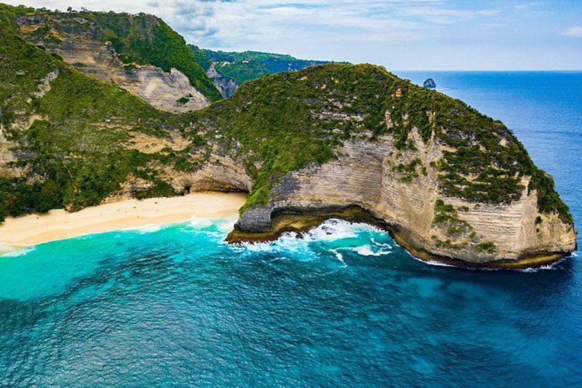 A coastal landscape with a prominent rock formation, a sandy beach, and clear blue waters. 2