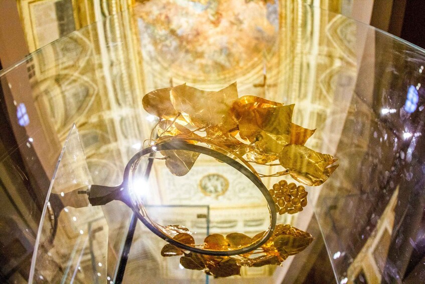 A glass display case with a golden, leaf-shaped object and a circular metal piece. 3