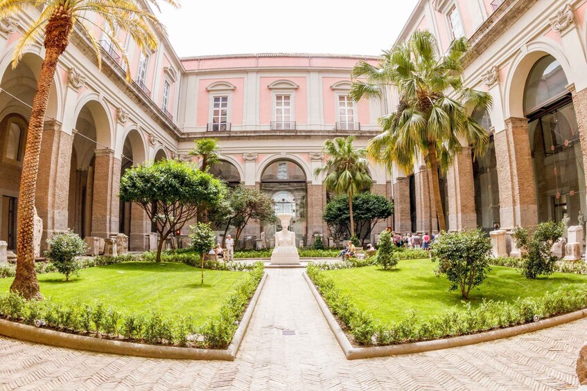 A courtyard with a central fountain, surrounded by palm trees and a brick building with arches. 5