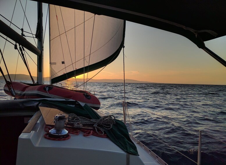 A sailboat with a red life preserver and a green cover on the deck, sailing on the ocean with a sunset in the background. 1