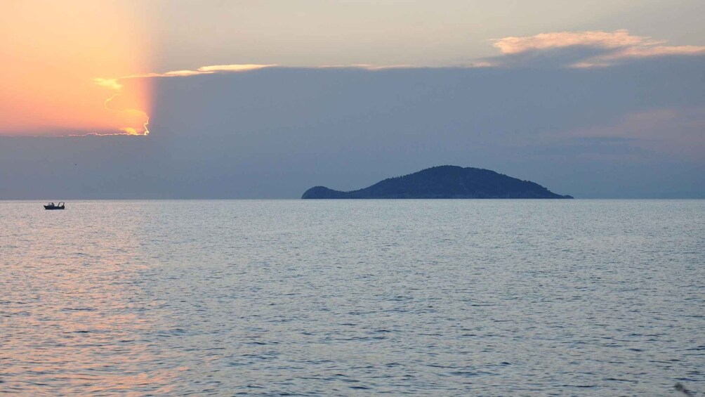 A calm sea with a small boat in the distance and a distant island silhouetted against the sky. 3