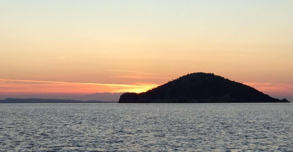 A sunset over a calm sea with an island silhouetted against the sky. 4