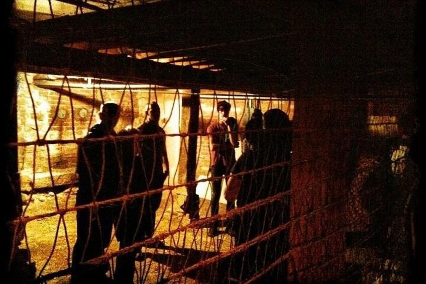 A group of people inside a dimly lit enclosure with a wire mesh roof, surrounded by a brick wall. 1