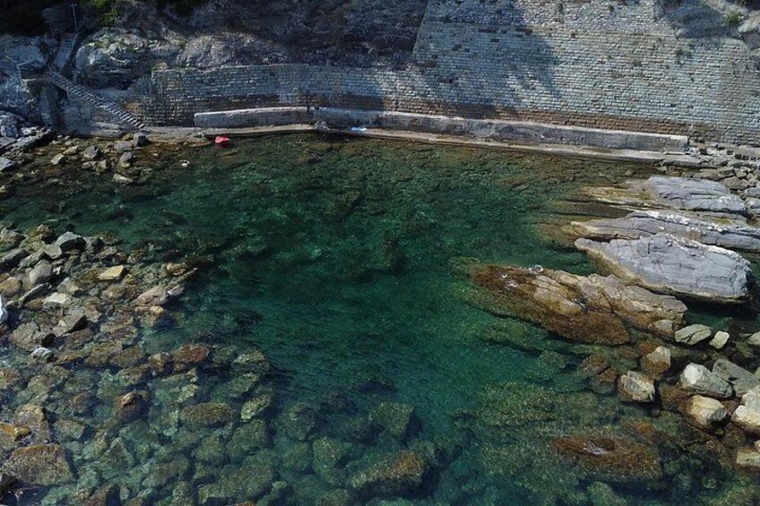 Una piscina cristalina con rocas y un muro de piedra al fondo. 4