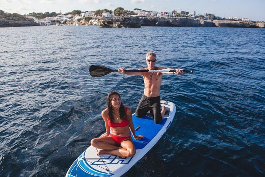 Two people on a paddleboard in the water, with a coastal town in the background. 2