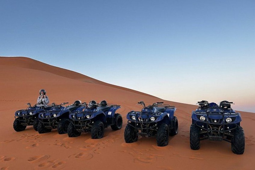 Four ATVs parked on a desert sand dune with a clear sky. 5