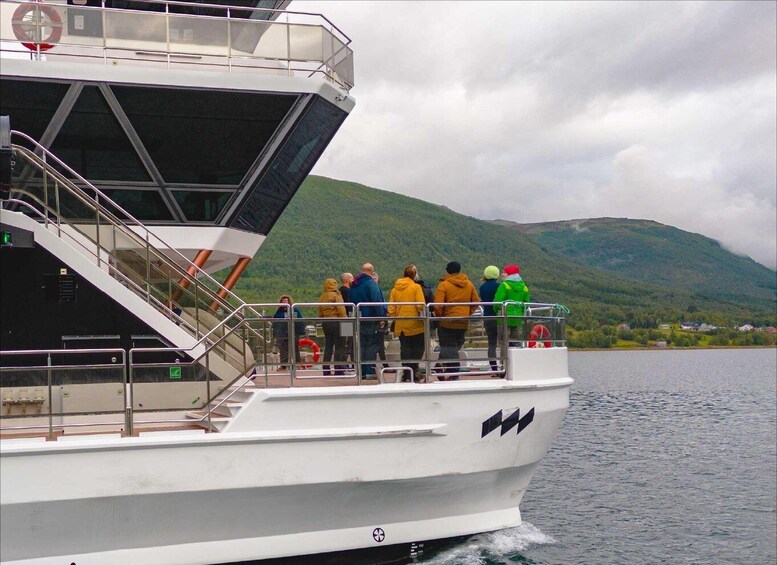 Een boot met mensen op het dek, een reddingsboei en een bergachtig landschap op de achtergrond. 5