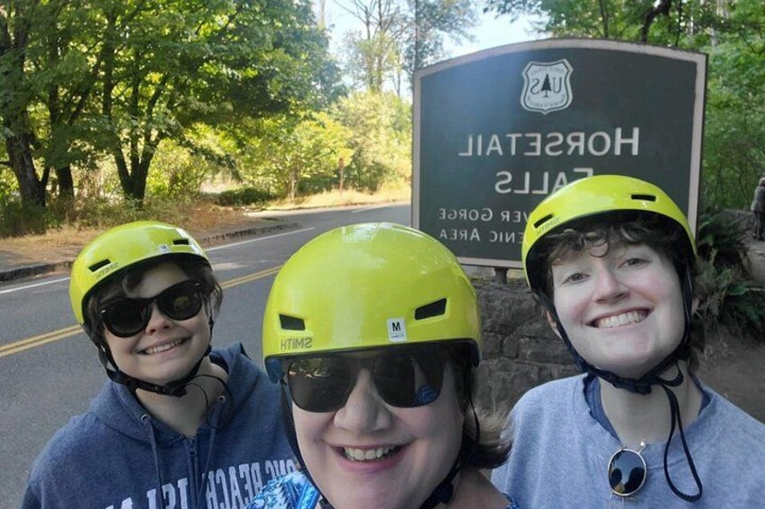 Three people wearing helmets, a road, and a sign that reads 'HOSPITAL' with a logo. 2