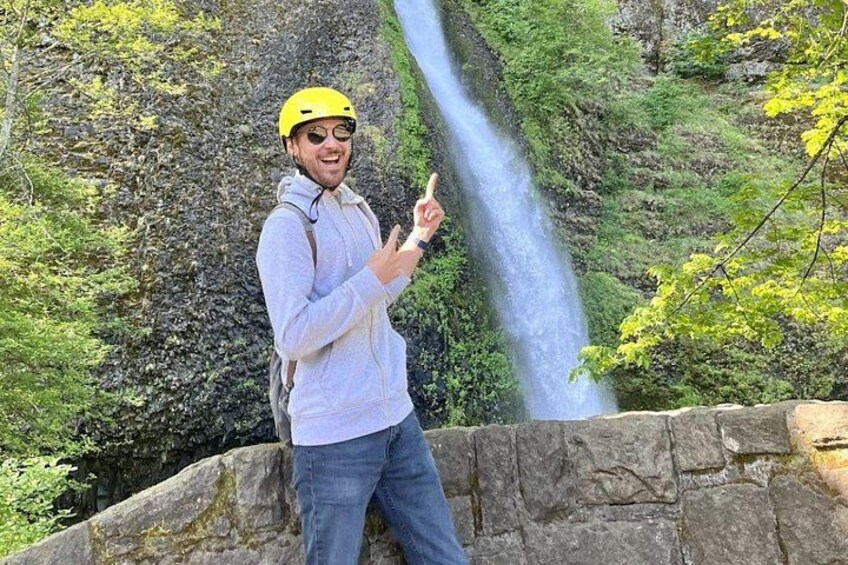 A person wearing a helmet and pointing at a waterfall. 4