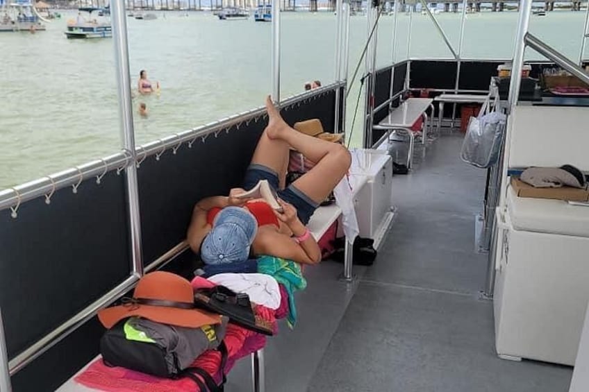 A boat with people resting on the deck, a water body in the background, and a small table with items on it. 5