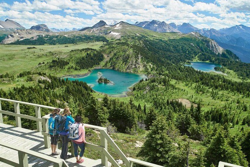 A mountainous landscape with a turquoise lake surrounded by dense forests and distant peaks. 2