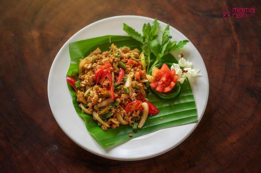 A plate of food with a banana leaf, red peppers, and a garnish of herbs and flowers. 5