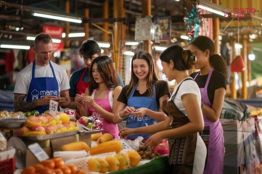 Eine Gruppe von Menschen an einem Marktstand, wo verschiedene Früchte und Gemüsesorten ausgestellt sind. 1
