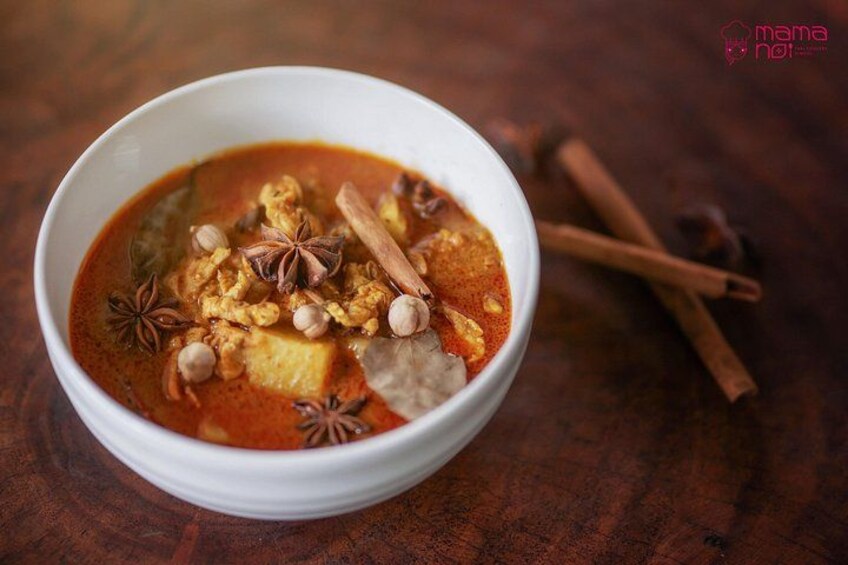 A bowl of curry with spices and nuts on a wooden table. 3