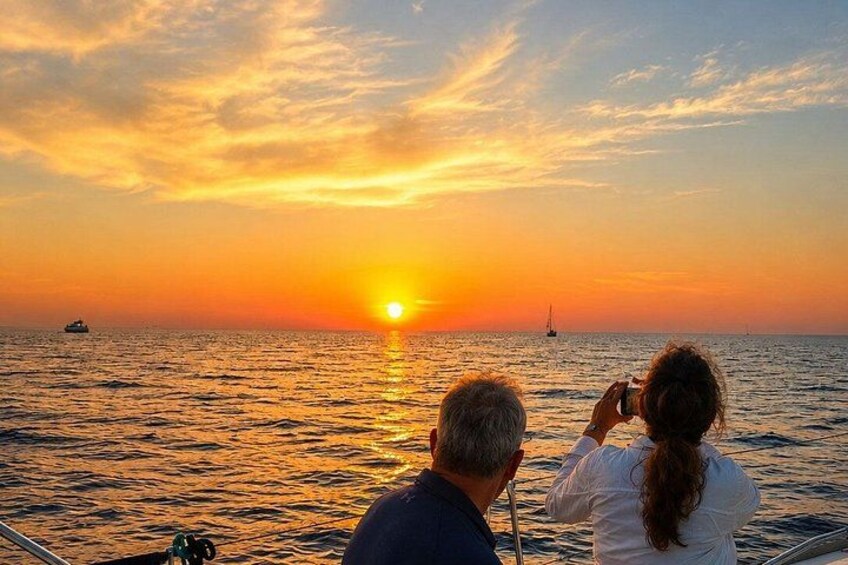 Un atardecer sobre el océano, con un barco y un velero a lo lejos. 3