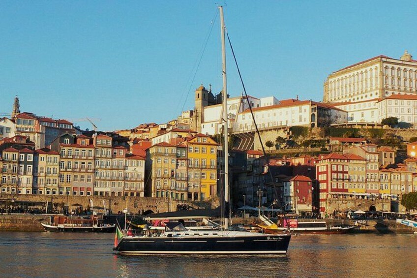 A river with a sailboat, buildings along the riverbank, and a prominent white building in the background. 1