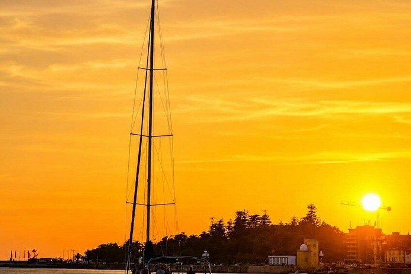 Un velero silueteado contra un atardecer con el perfil urbano de una ciudad al fondo. 5