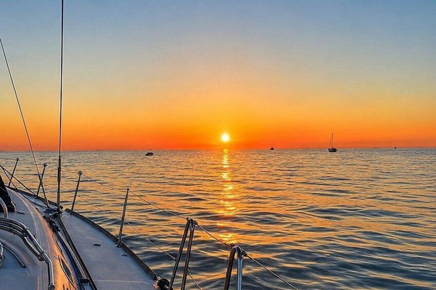 Un atardecer sobre aguas tranquilas con la proa y el mástil de un barco en primer plano. 2